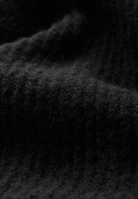 Tessuto nero texturizzato con un aspetto morbido e peloso. Presenta un motivo a costine con spessori variabili, che conferiscono profondità e dimensione.