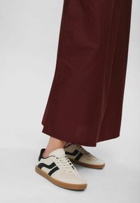 Baskets basses crème avec des accents noirs et des panneaux en maille texturée. Associées à un pantalon large bordeaux.