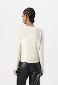Pull en tricot couleur crème à manches longues et encolure ronde, avec une texture douce et une coupe décontractée, associé à un pantalon noir.