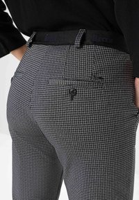 Hoch geschnittene graue karierte Hose aus strukturiertem Stoff, mit einem schwarzen Bund, Gesäßtaschen und einem Knopfdetail.
