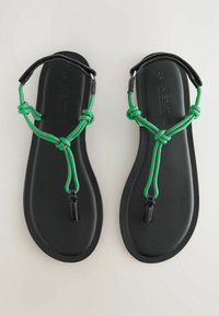 Zwarte teenslippers met een bovenzijde van groen en roze gevlochten koord met knopen, verbonden door zwart beslag, en gevormde platte zolen.