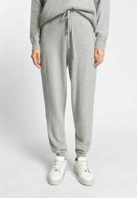 Graue Strick-Jogginghosen mit Kordelzug, versehen mit vertikalen Nähten und Bündchen am Knöchel, kombiniert mit weißen Schnürsneakern.