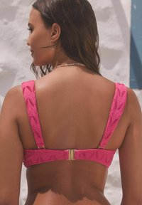 Fuchsia kant zwem-bh met brede bandjes, ingewikkelde patronen en een goudkleurige sluiting aan de achterkant. Soepele textuur tegen de huid.