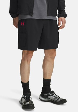 Pantaloni cargo neri con logo Under Armour rosa, realizzati in materiale leggero. Presentano tasche laterali, abbinati a sneaker nere e grigie con calze.