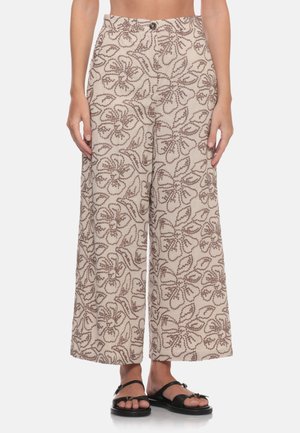 Pantaloni beige a gamba larga con motivi floreali e foglie marroni, indossati con sandali neri aperti davanti.
