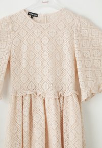 Vestido de encaje en rosa suave, con un patrón de diamantes, escote redondo, mangas abullonadas y una cintura con volantes, con cierre de cremallera en la parte posterior.