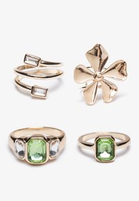 Quatre bagues : deux bagues en ton or avec des gemmes rectangulaires et rondes, une bague en forme de trèfle doré, et une bague avec une pierre verte ornée d'accents clairs.