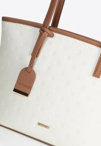 Witte gestructureerde tote bag met bruin leren details en handvatten. Bevat gegraveerde patronen en een gouden logo plaatje.