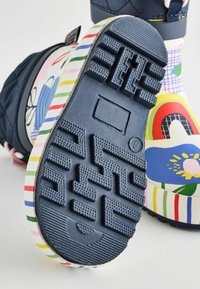 Bottes en caoutchouc colorées avec une tige bleue, semelle à motifs rayés et semelle texturée pour une meilleure adhérence. Présente des designs floraux et abstraits.