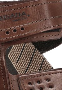 Sandalia de piel marrón con perforaciones, correa ajustable y plantilla texturizada con un diseño tipo malla.