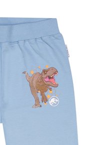  Lichtblauwe joggingbroek met een afbeelding van een brullende T-Rex met oranje accenten en een Jurassic Park-logo onderaan. Zacht katoenen materiaal.