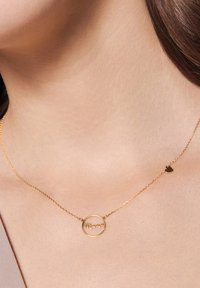 Złoty naszyjnik z okrągłym wisiorkiem z napisem "Mama" oraz małym charms'em w kształcie serca. Łańcuszek jest delikatny, o subtelnej strukturze.