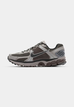 Light grey and dark brown running shoe with mesh detailing, structured design, and thick rubber sole. Features Nike swoosh logo and textured accents.