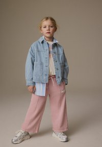 Randig blå denimjacka över en ljus grafisk t-shirt, tillsammans med rosa vida sweatpants och metalliska sneakers.