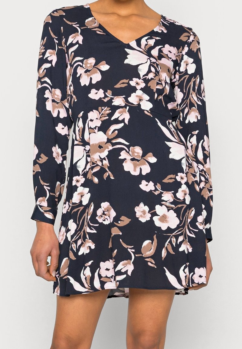 Vestito floreale con base blu navy, caratterizzato da fiori rosa e beige. Maniche lunghe, scollo a V e silhouette svasata. Tessuto dalla texture morbida.