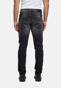 Mustat denim-haalareet kapenevalla istuvuudella, joissa on erottuvat ompeleet, kaksi takataskua ja sileä pinta. Yhdistettynä valkoiseen paitaan.