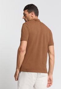 Bruine poloshirt met korte mouwen, voorzien van een klassieke kraag en een gladde, gestructureerde stof. De achterkant toont een strak ontwerp.