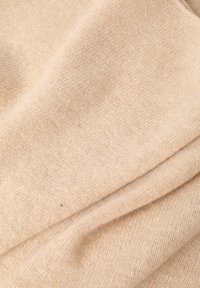 Béžová pletená tkanina s měkkou texturou, obsahující malé kovové flí�čky. Materiál působí teple a útulně, s mírně nerovnoměrným vazbou.