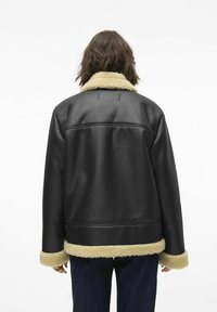 Veste en cuir noir avec un col et des poignets en fausse fourrure beige. Présente une coupe décontractée et des coutures visibles à l'arrière.