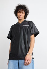 T-shirt preto de manga curta com design em V, feita de tecido suave, com um logo Adidas branco em destaque e detalhes em rede.