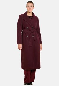Burgundská vlnená trench coat s dvojitým predným zapínaním, širokým golierom, opaskom a zodpovedajúcimi nohavicami. Hladká textúra a prispôsobený strih.