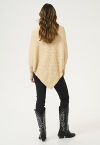 Crème poncho cardigan met zigzagpatroon, gecombineerd met zwarte skinny jeans en hoge zwarte cowboylaarzen met ingewikkelde zilveren borduursels.