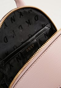 Růžová texturovaná kožená kabelka s zlatým zipem a černým interiérem s vzorem loga DKNY a malou cedulkou.