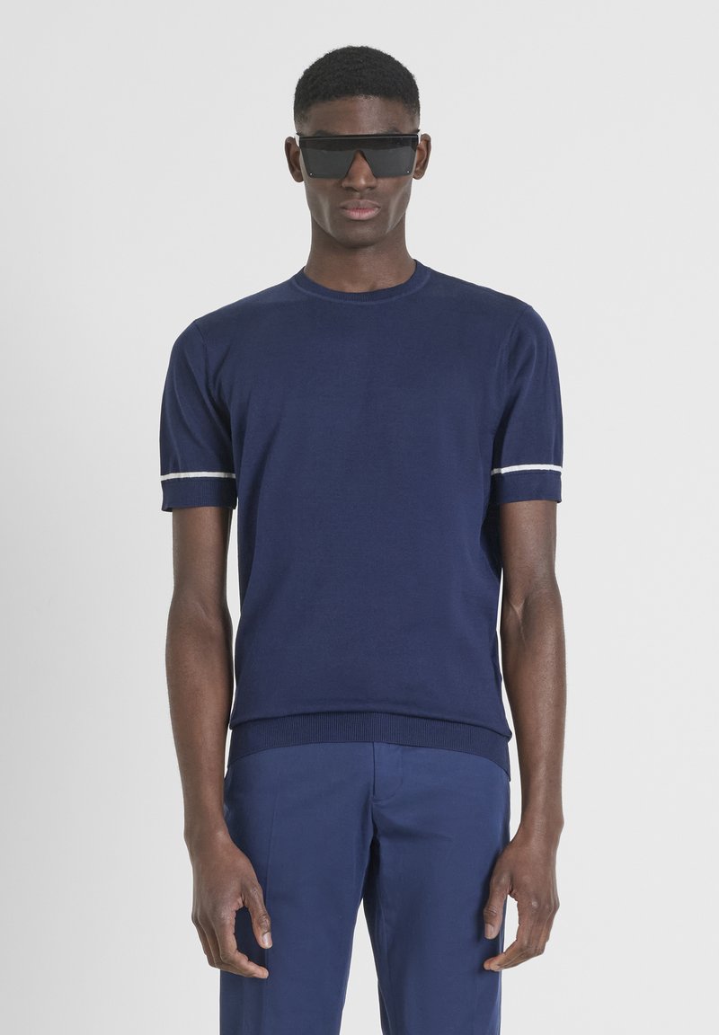 Maglietta a maglia blu navy con maniche corte, caratterizzata da strisce bianche sulle maniche. Collo a giro, orlo rigato, texture liscia, design aderente.