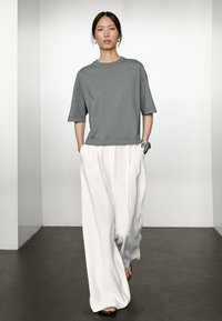 T-shirt gris surdimensionné à manches courtes, associé à un pantalon large blanc, avec une coupe décontractée et des textures lisses. Design simple.