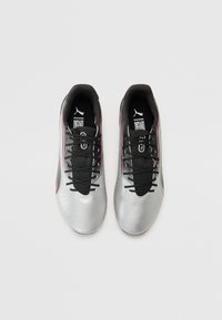 Baskets de sport argentées avec des accents noirs, texture lisse, design à lacets, bordure rose notable, et un logo sur la languette et la semelle.