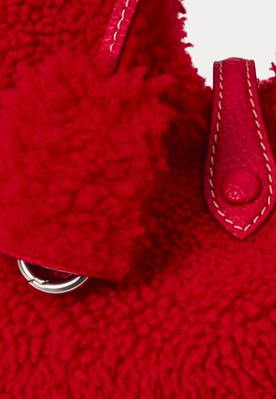 Červená texturovaná taška s huňatým vnějším materiálem a koženými doplňky. Obsahuje stříbrný kovový kroužek a prošité detaily na popruzích.