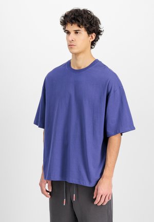 Lilla oversized bomulds T-shirt med korte ærmer og rund halsudskæring, der har en glat tekstur og løs pasform, kombineret med grå bukser.