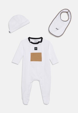 Ensemble pour bébé blanc avec un body à manches longues avec pieds, un bonnet assorti et un bavoir blanc avec bordure noire et détails du logo.