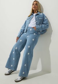 Ruutuhousut ja leveät farkut, joissa on valkoisia päivänkakkaroita, vaaleansininen väri, kontrastiväriset ompeleet, yhdistettynä musti-valkoisiin lenkkarite.