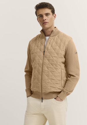 Beige gesteppte Sweatjacke mit hohem Kragen, Reißverschluss und elastischen Bündchen. Glatte Textur mit geripptem Saum und Seitentaschen.