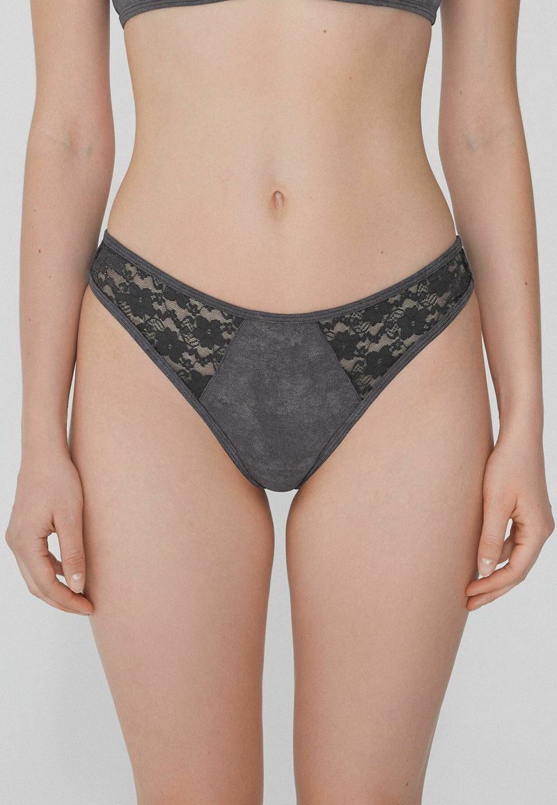 Ropa interior gris que presenta una combinación de tejido suave y delicado encaje negro en los laterales, con forma triangular y cinturilla.