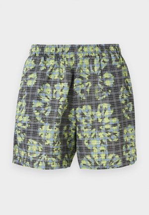 Shorts med elastisk midje i grå rutete mønster og stort abstrakt grønt og blått blomstermotiv, vist mot en ensfarget bakgrunn.