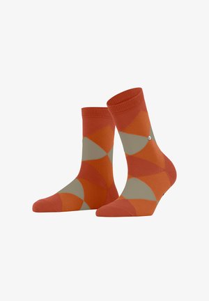 Orange and beige patterned socks with a geometric design. Made of soft material, featuring ribbed cuffs and a decorative metal accent.