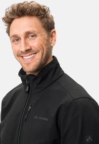 Čierna softshell bunda s vysokým golierom, predným zipsom a náprsnom vreckom. Má hladkú textúru a nenápadný detail loga.