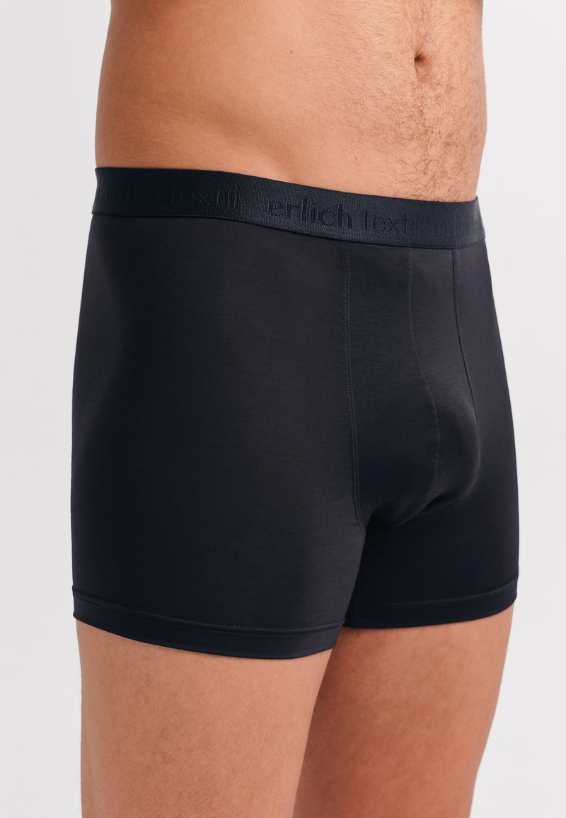 Schwarze Boxershorts aus einem glatten, dehnbaren Material. Verfügt über einen weichen elastischen Bund mit dem Text "erlich textil" in einer tonal abgestimmten Farbe.