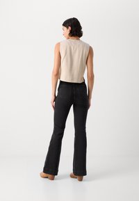 Bijgesneden beige mouwloze top gecombineerd met zwarte flared jeans, voorzien van zakken en een rechte tailleband; gedragen met tan kleurige hakken.