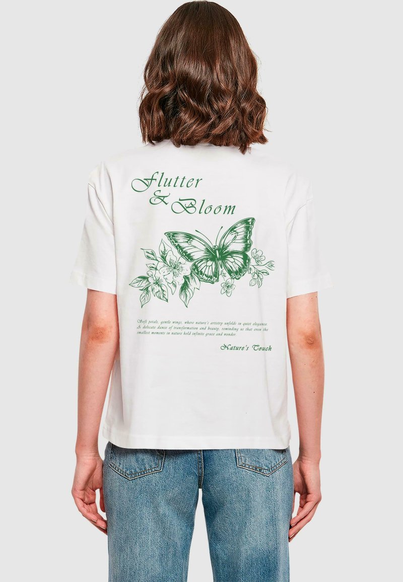 Hvid bomulds T-shirt med grønne sommerfugl- og blomstermotiver på bagsiden samt teksten "Flutter & Bloom" i en elegant skrifttype.