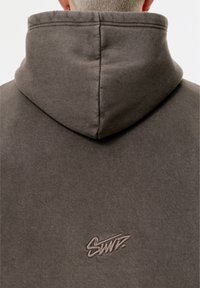 Sweat à capuche gris à texture douce, avec un petit logo brodé de couleur plus claire dans le dos.