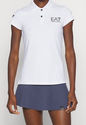 Mujer que lleva una camiseta polo blanca EA7 Emporio Armani y una falda de tenis azul marino texturizada con el logo de Endless.