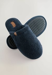 Navyblaue Hausschuhe aus plüschigem Material mit weicher Textur, ausgestattet mit einer Gummisohle mit horizontalen Rillen und einem braunen Lederakzent.