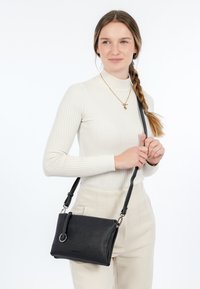 Borsa a tracolla in pelle nera con superficie texturizzata, dotata di una tracolla removibile e di un accento circolare sulla parte anteriore.