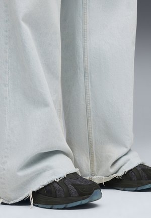 Ljusblå, vida denimbyxor med fransade fållar. Svarta sportskor med texturerade detaljer och en solid sula under byxorna.