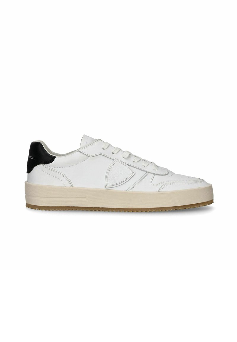 Sneaker en cuir blanc avec un accent noir au talon, surface texturée, bout arrondi, lacets plats et semelle en caoutchouc surélevée.