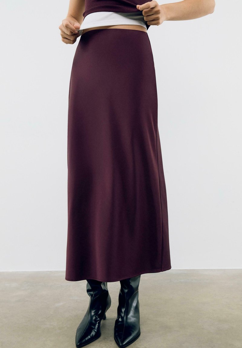 Bordeaux maxi rok van soepel, rekbaar materiaal met een hoge tailleband, gecombineerd met zwarte puntige kniehoge laarzen.
