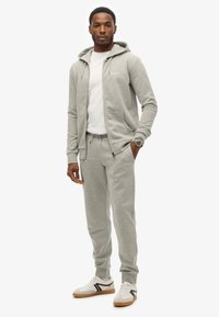 Lysegrå zip-up hættetrøje med en hvid T-shirt underneath, parret med matchende joggers og hvide sneakers med sorte accenter.